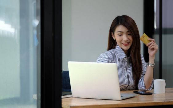 Asian girl making online payment using laptop for shopping at home, famle holding credit card.