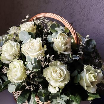 Bouquet of beautiful white roses in a wicker basket on a dark background. Perfect for greeting card