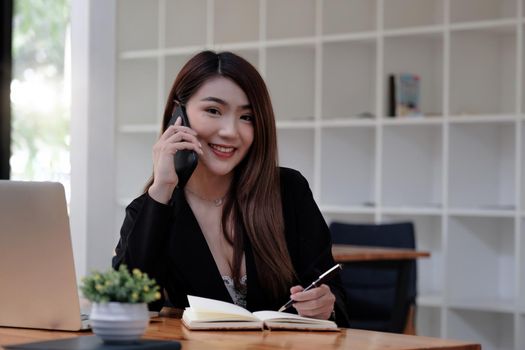 Asian business woman making a phone call and smiling look at camera. secretary famale taking note during call consultant.