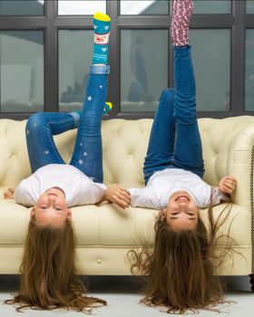 Pretty girls are lying on their backs on the couch, looking at the camera and smiling, playing at home.