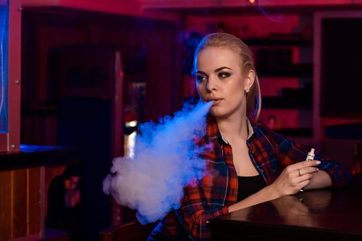 Young pretty woman in a shirt in a cage smoke an electronic cigarette at the vape bar. Vape shop.
