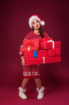 Young woman in dress and christmas hat holding gift boxes on red background. Christmas sale. Emotional brunette. Copy space