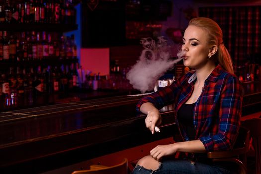 Young pretty woman smoke an electronic cigarette at the vape bar. Vape shop.