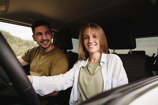 Beautiful young smiling couple sitting on front passenger seats and driving a car