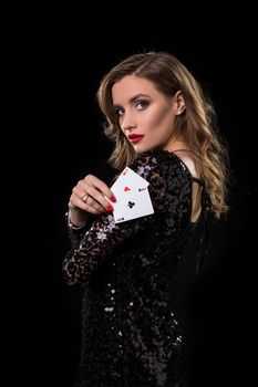 Young beautiful woman in black shiny dress holds poker cards in hands against a black background. The concept of gambling. Casino