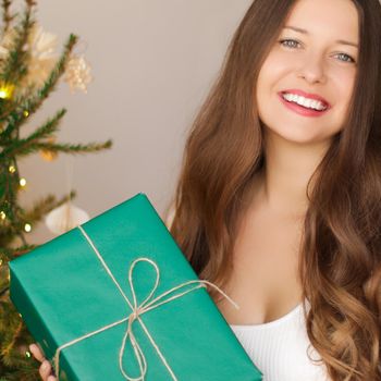 Christmas holiday and sustainable gifts concept. Happy smiling woman holding wrapped present with eco-friendly green wrapping paper.
