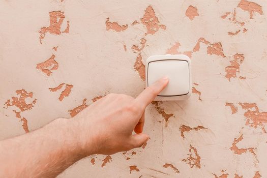 The guy's hand turns off the light with an electric switch in a modern room interior background.