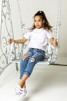 Beautiful little girl swinging in the studio on a swing. Concept of a happy childhood, family well-being.