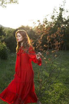 woman in red dress in field near tree posing summer. High quality photo