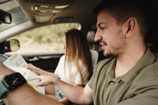 Young loving couple on a road trip using map inside a car, close up