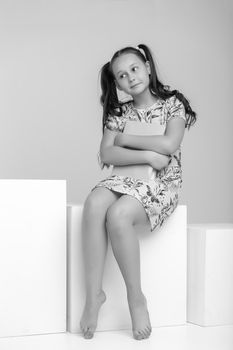 Beautiful little girl sitting on a white staircase and reading a book. The concept of children's literature.