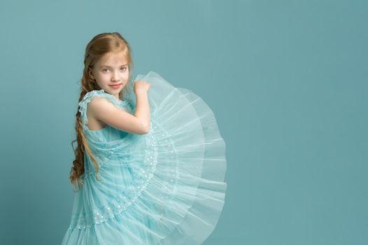 Beautiful little girl in an elegant dress holds her hands around the edges of the skirt.