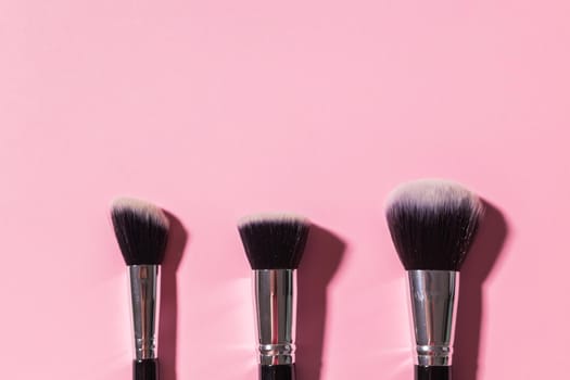 Various make-up brushes on pink background, top view. Cosmetics and beauty