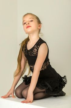 Beautiful little girl poses for a magazine in the studio on a white cube.