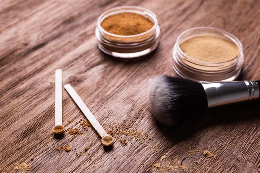 Mineral powder of different colors with spoon dispenser for make-up on wooden background.