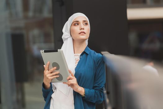 Smiling muslim girl using digital tablet, browsing Internet or social networks outdoor.