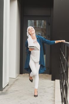 Smiling muslim girl using digital tablet, browsing Internet or social networks outdoor.