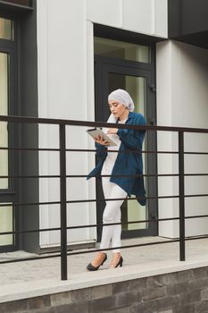 Smiling muslim girl using digital tablet, browsing Internet or social networks outdoor.