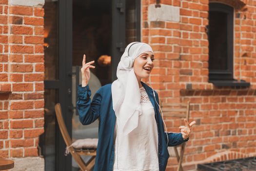 Portrait of young arabian muslim woman listening music with headphone and dancing. Feminism, woman independence and leisure concept