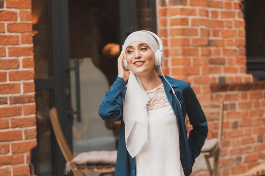 Portrait of young modern arabian woman holding mobile phone and listening the music to headphone