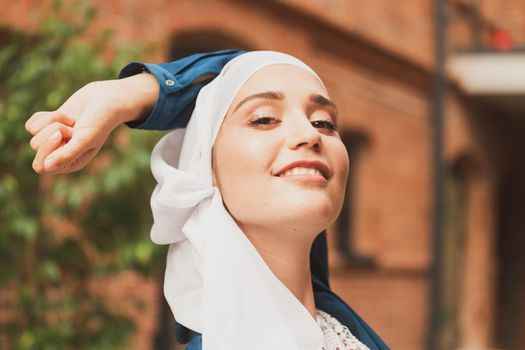 Portrait of young muslim woman wearing hijab head scarf in city while looking at camera. Closeup face of cheerful woman covered with headscarf smiling outdoor. Islamic girl outdoors