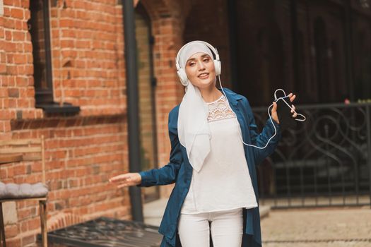 Portrait of young arabian muslim woman listening music with headphone and dancing. Feminism, woman independence and leisure concept