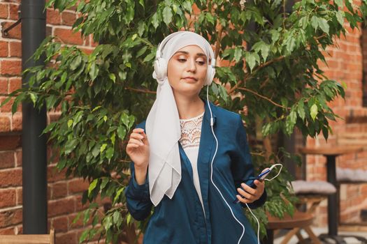 Portrait of young modern arabian woman holding mobile phone and listening the music to headphone