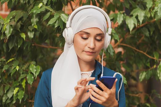 Portrait of young modern arabian woman holding mobile phone and listening the music to headphone