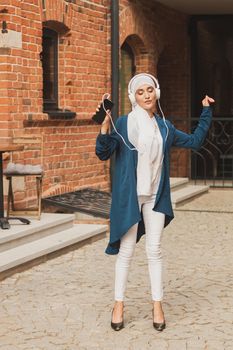 Portrait of young arabian muslim woman listening music with headphone and dancing. Feminism, woman independence and leisure concept