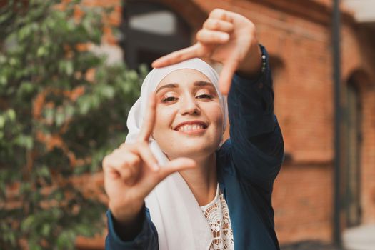 Portrait of young muslim girl making a camera frame with fingers outdoors