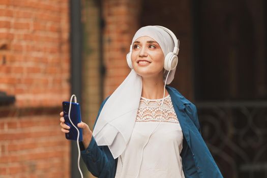 Portrait of young modern arabian woman holding mobile phone and listening the music to headphone
