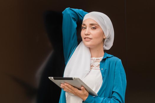 Smiling muslim girl using digital tablet, browsing Internet or social networks outdoor.