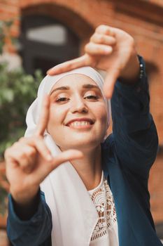 Portrait of young muslim girl making a camera frame with fingers outdoors