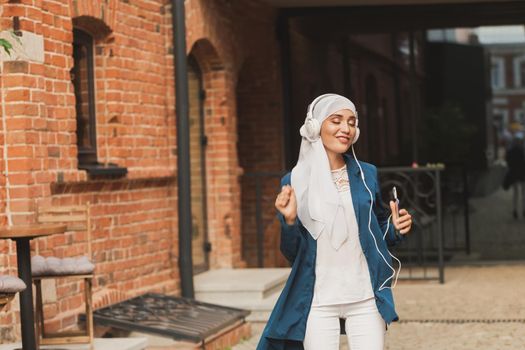 Portrait of young arabian muslim woman listening music with headphone and dancing. Feminism, woman independence and leisure concept