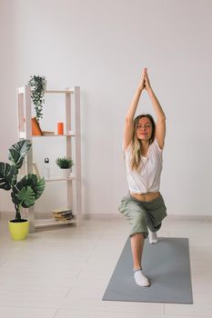 Woman practise yoga performs. Pose on mat inside of cozy room with plants and greenery. Healthy lifestyle