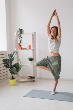 Woman practise yoga performs. Pose on mat inside of cozy room with plants and greenery. Healthy lifestyle