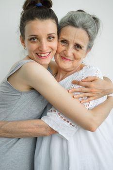 Happy senior mother is hugging her adult daughter, the women are laughing together, sincere family of different age generations having fun on white background, mothers day