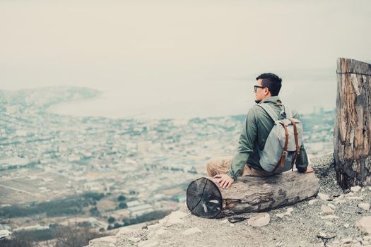 Tourist young man sitting on tree trunk and looking at town