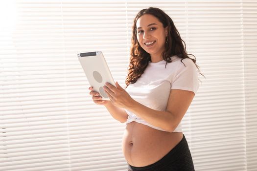 Happy pregnant young beautiful woman talking to her husband using video connection and tablet. Communication and positive attitude during pregnancy