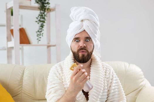 Bearded male with bath towel on his head applying spray water treatment on face. Spa, body and skin care for man concept