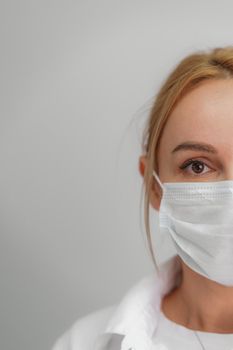 Close-up portrait of a young blonde woman in a medical mask on a light background. Virus protection. Coronovirus covid-19 The concept of a pandemic epidemic. Quarantine. Stay at home