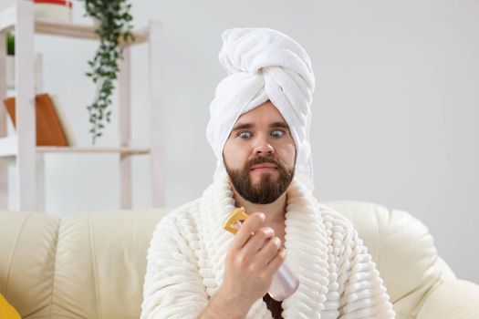 Bearded male with bath towel on his head applying spray water treatment on face. Spa, body and skin care for man concept
