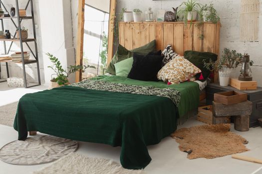 Comfortable bed with new green linens in eco style room interior.