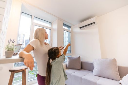 Happy family under air conditioner, mom holding remote control switch on conditioning in living room adjust comfort temperature for daughter, climate system at modern home