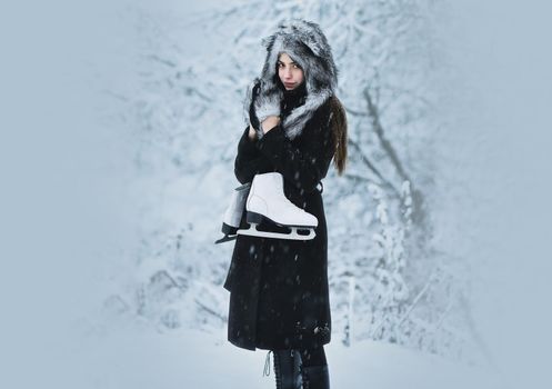 Girl with figure skates at trees in snow. Woman with skating shoes in winter clothes in snowy forest. Winter vacation, holidays and lifestyle.