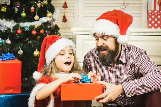Happy Father and daughter child with present gift in santa hat at Christmas tree. Winter family holiday and happy New year.