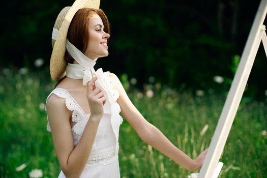 Woman in white dress paints a picture on nature easel. High quality photo