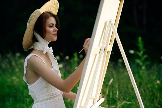 Woman in white dress paints a picture on nature easel. High quality photo