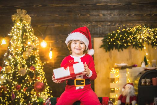 Portrait of funny kid with gift looking at camera. Kid having fun near Christmas tree indoors