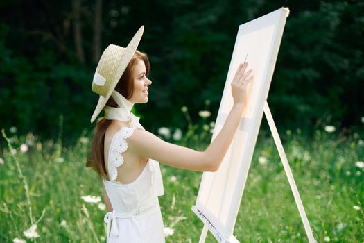 Woman in white dress in nature paints a picture of a landscape hobby. High quality photo